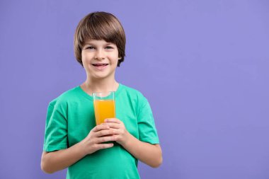 Menekşe arka planında bir bardak taze portakal suyu olan çocuk. Metin için boşluk