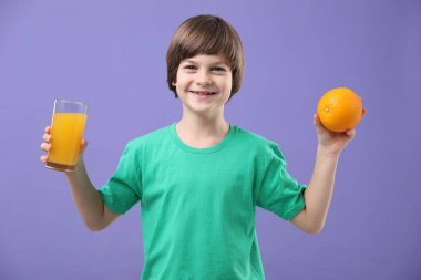 Menekşe arka planında bir bardak taze portakal suyu ve meyvesi olan çocuk.