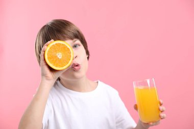 Pembe arka planda bir bardak taze portakal suyu ve meyvesi olan çocuk. Metin için boşluk