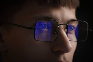 Siyah arka planda yansıması olan gözlüklü genç adam, yakın plan.