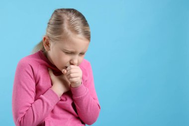 Küçük kız açık mavi arka planda öksürüyor, mesaj için yer var. Soğuk Semptom