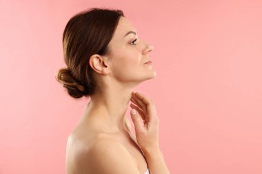 Kadın pembe arka planda boynuna dokunuyor.