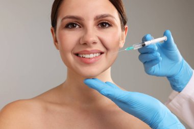 Estetik ameliyat. Doktor gri arka plandaki hastaya yüz enjeksiyonu yapıyor.