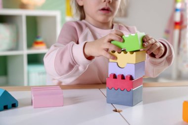 Oyun odasındaki beyaz masada oyuncaklarla oynayan mutlu küçük kız, yakın plan.