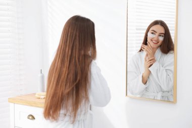 Banyoda aynanın yanında göz bantları olan bornozlu güzel bir kadın.