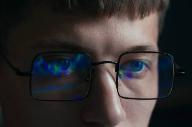 Siyah arka planda yansıması olan gözlüklü genç adam, yakın plan.