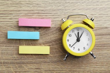 Blank notes and alarm clock on wooden table, flat lay