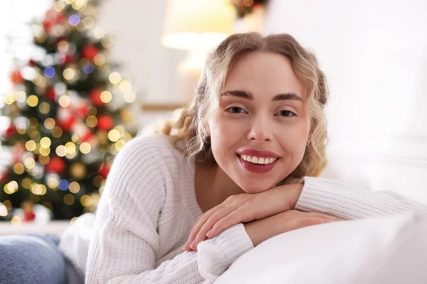 Evdeki bulanık ışıklara karşı kanepede süveter giymiş gülümseyen kadın portresi. Mutlu Noeller ve mutlu yıllar.