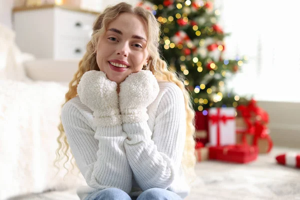 Evdeki bulanık ışıklara karşı eldivenli ve kazaklı gülümseyen kadın portresi. Mutlu Noeller ve mutlu yıllar.