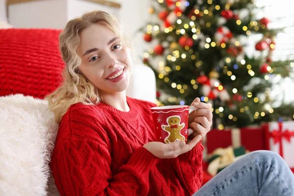 Evde bulanık ışıklara karşı elinde bir fincan sıcak içecekle gülümseyen kadın portresi. Mutlu Noeller ve mutlu yıllar.