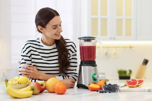 Mutfakta meyve ve blender ile beyaz mermer masada gülümseyen kadın.