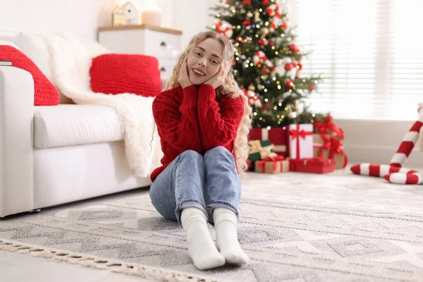 Yerde süveter giymiş gülümseyen bir kadın. Odadaki bulanık ışıklara karşı. Noel için süslenmiş.