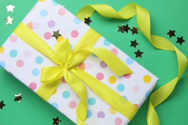 Yeşil arka planda yay ve yıldız şekilli konfeti ile sarılı güzel bir hediye.