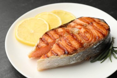 Biberiye ve limonlu ızgara somon bifteği siyah masada, yakın plan.