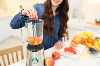Gülümseyen kadın, beyaz masada mikserle enfes bir smoothie hazırlıyor.