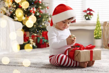 Noel Baba şapkalı küçük çocuk Noel için dekore edilmiş odada yerde hediyeyle