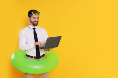Dalış maskesi, dizüstü bilgisayarı ve turuncu arka planda şişirilebilir yüzüğü olan bir iş adamı.