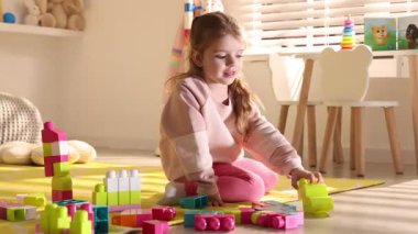 Küçük kız oyun odasında yerde oyuncaklarla oynuyor.