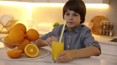 Çocuk mutfaktaki masada taze portakal suyu içiyor.