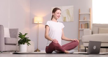 Hamile bir kadın evde dizüstü bilgisayarla yoga dersi alıyor.