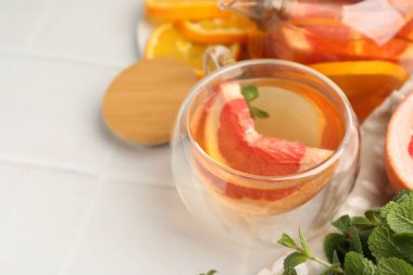 Cam fincanda aromatik meyve çayı, çaydanlık, portakal greyfurtu ve beyaz fayanslı masada nane şekeri, yakın plan. Metin için boşluk