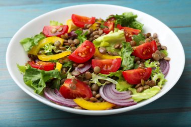 Açık mavi ahşap masada mercimek ve sebzeli nefis salata, yakın plan.