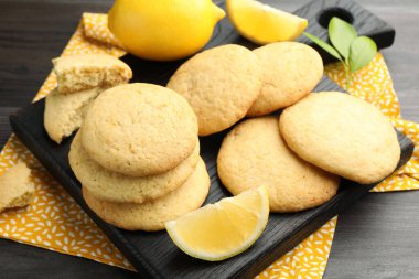 Lezzetli limonlu kurabiyeler ve koyu ahşap masadaki meyve dilimleri, yakın plan.
