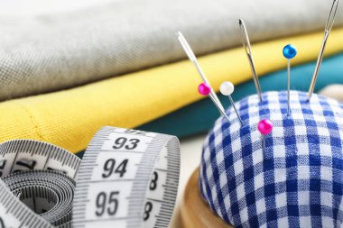 İğneler, iğneler, kumaşlar ve mezura ile kareli iğne, yakın plan.