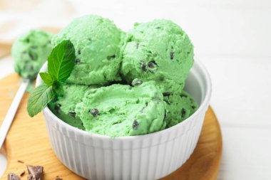 Çikolata parçalı lezzetli dondurma ve kaşık beyaz ahşap masada, yakın plan.