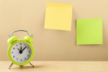Üzerinde yapışkan notlar olan bej duvarın yanındaki ahşap masadaki çalar saat. Metin için boşluk