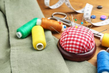 İğneler, iğneler, kumaşlar ve iplikçikler ile ahşap masada kareli iğnelik, yakın çekim