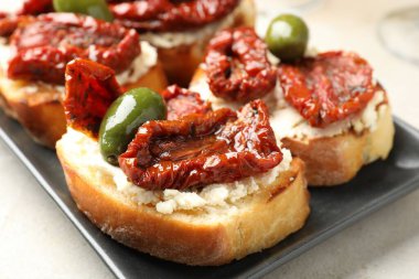 Krem peynirli lezzetli bruschettalar, güneşte kurutulmuş domatesler ve gri masada yeşil zeytinler, yakın plan.