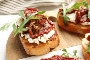 Krem peynirli lezzetli bruschettalar, güneşte kurutulmuş domatesler ve masanda roka, yakın plan.