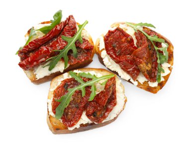 Krem peynirli lezzetli bruschettalar, güneşte kurutulmuş domatesler ve beyaza izole edilmiş roka.