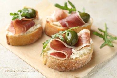 Krem peynirli lezzetli bruschettalar, prosciutto, yeşil zeytin ve roka gri masada, yakın plan.