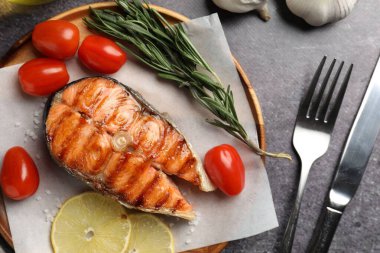 Lezzetli ızgara somon bifteği, limon, domates ve biberiye ile servis edilir.