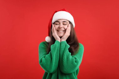 Kırmızı arka planda Noel Baba şapkalı güzel bir kadın. Noel sezonu