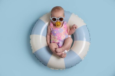 Güneş gözlüklü şirin küçük bebek ve şişirilebilir halka üzerinde emzik açık mavi arka plan, üst görünüm