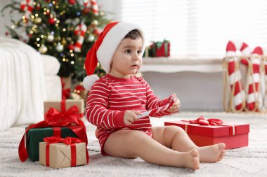 Noel Baba şapkalı küçük çocuk Noel için dekore edilmiş odada yerde hediyeler taşıyor.