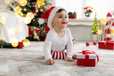 Noel Baba şapkalı küçük çocuk Noel için dekore edilmiş odada yerde hediyeyle