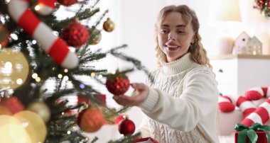 Evdeki Noel ağacına süveter giyen gülümseyen kadın güzel bir takı takıyor. Bokeh etkisi