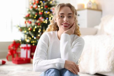 Evdeki bulanık ışıklara karşı süveter giymiş gülümseyen kadın portresi. Mutlu Noeller ve mutlu yıllar.