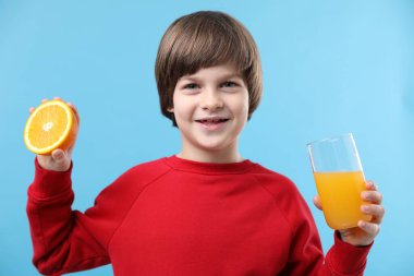 Açık mavi arka planda taze portakal suyu ve meyvesi olan bir çocuk.