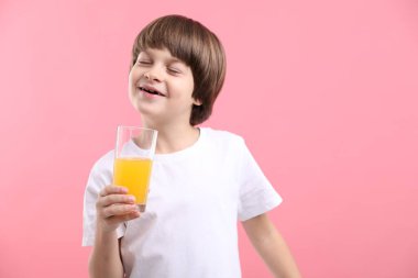 Pembe arka planda bir bardak taze portakal suyu olan çocuk. Metin için boşluk
