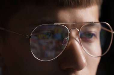 Siyah arka planda yansıması olan gözlüklü genç adam, yakın plan.