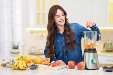 Gülümseyen kadın mutfaktaki beyaz mermer masada blender ile nefis smoothie yapıyor. Metin için boşluk