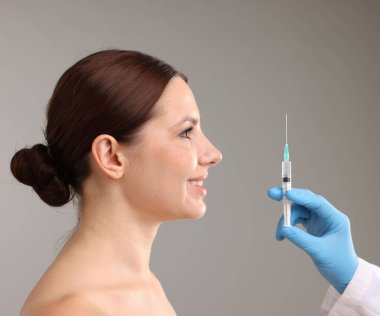 Estetik ameliyat. Doktor gri arka plandaki hastaya yüz enjeksiyonu yapıyor.