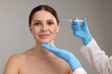 Estetik ameliyat. Doktor gri arka plandaki hastaya yüz enjeksiyonu yapıyor.