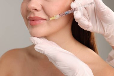 Doktor, gri arka plandaki hastaya yüz enjeksiyonu yapıyor. Yakın plan. Estetik ameliyat