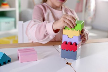 Oyun odasındaki beyaz masada oyuncaklarla oynayan mutlu küçük kız, yakın plan.